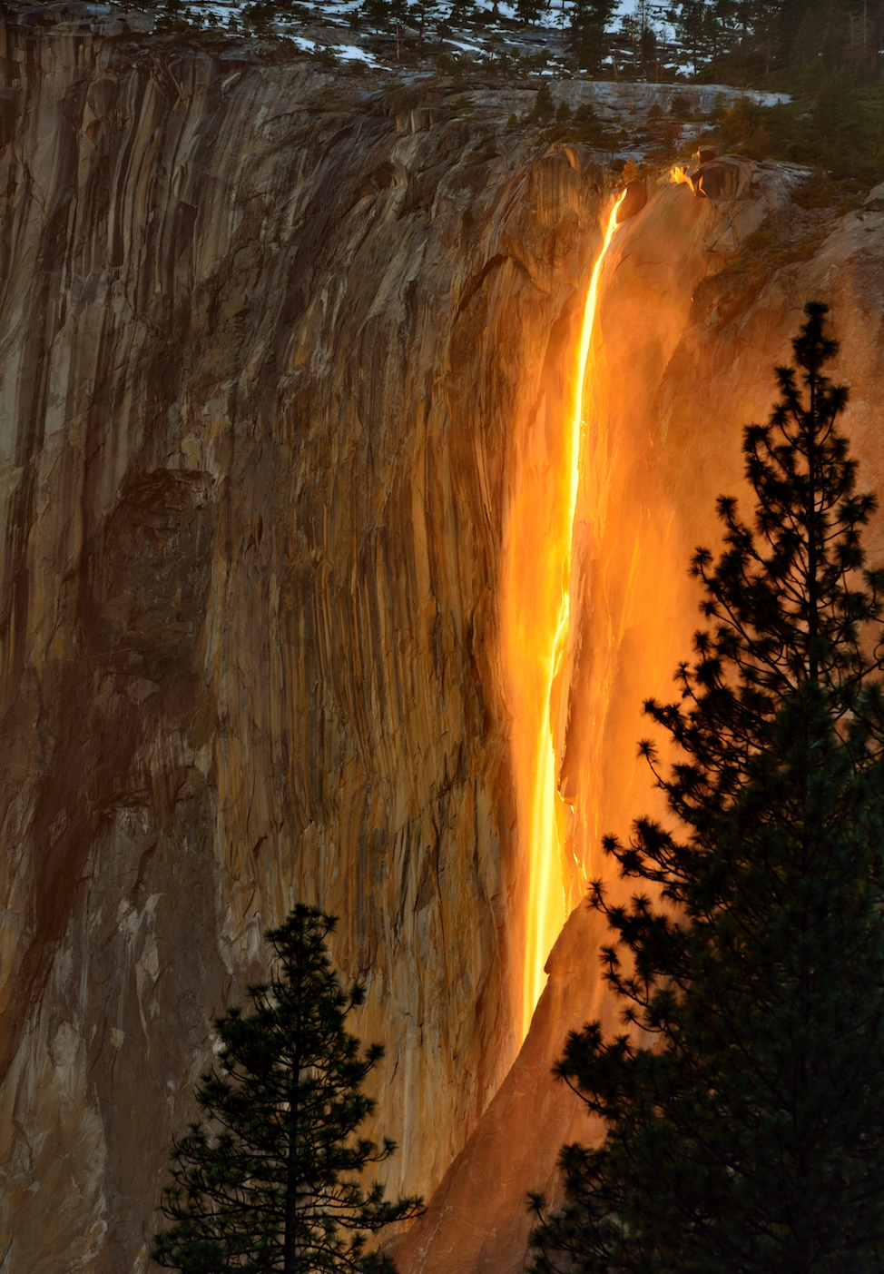 A waterfall glows orange down the side of a granite formation.