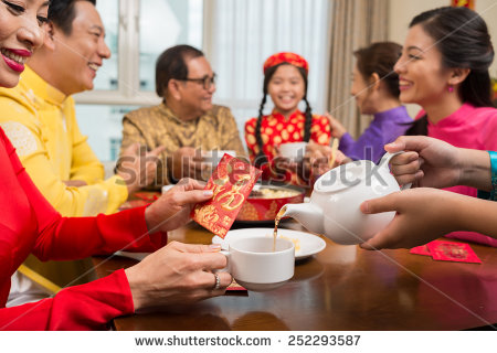 Hands pouring tea in a cup on the background of family celebrating Tet