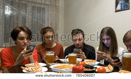 Group of friends at dinner party with all people on the table occupied with cellphones. friends with smartphones dining at home. technology and internet addiction concept
