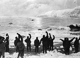 A black-and-white photograph of a group of men waving to something in the distance
